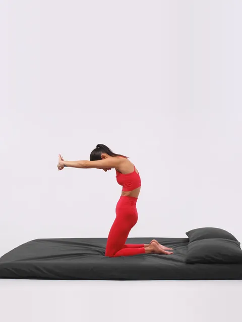 A woman kneeling on a mattress, reaching both arms forward