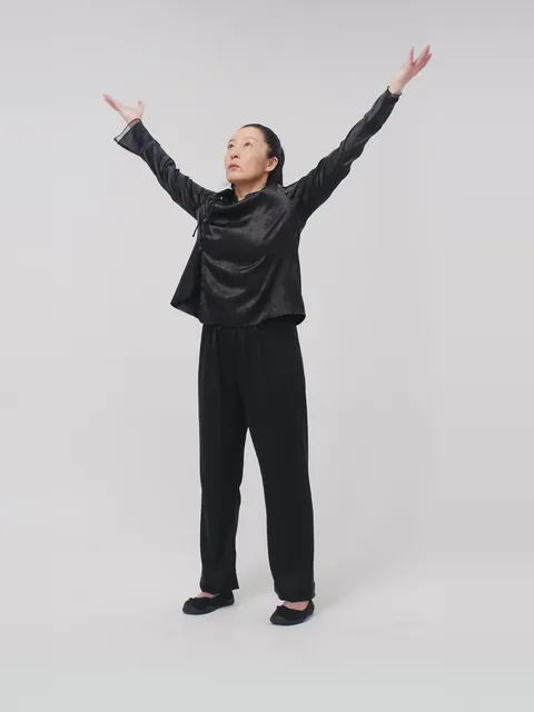 A woman in a qigong pose with both arms raised wide