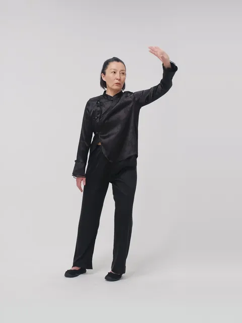 A woman in a black tai chi suit with one arm raised in a slow form